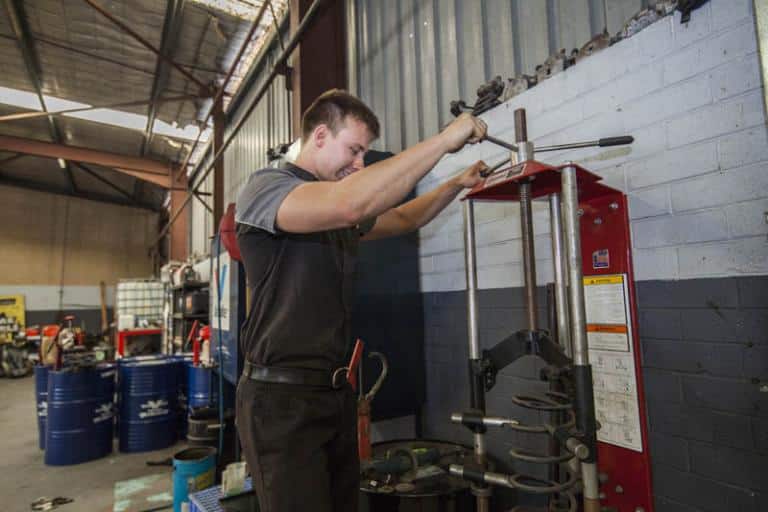 smiling auto mechanic repairing vehicle coil suspension in machine in adrian's balcatta car care center