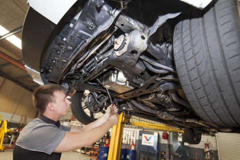 mechanic standing underneath car on lift in service centre loosening the samp