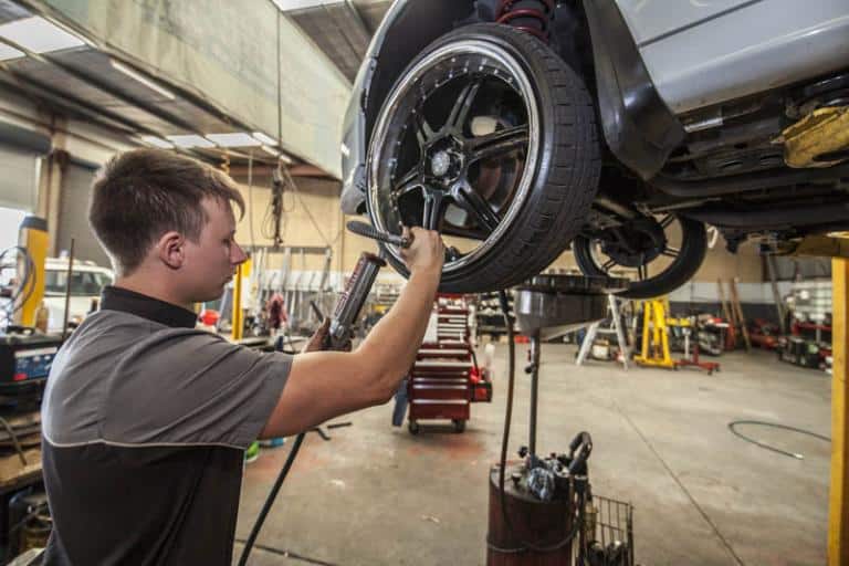 mechanic standing next to car on a lift checking the front wheel tire pressure