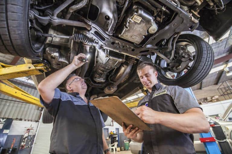 mechanics examining the underneath of a car in service centre while it is on a car lift writing down what they see