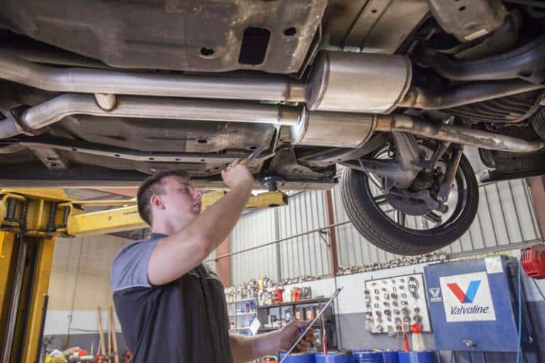 young male mechanic examining the system of a car in service centre while it is on a car lift