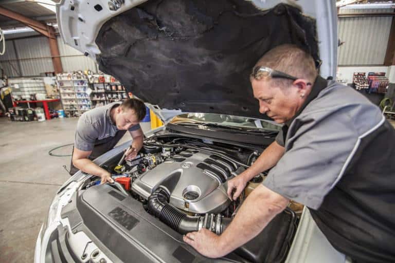 professional car mechanics looking under car hood to inspect the engine while servicing