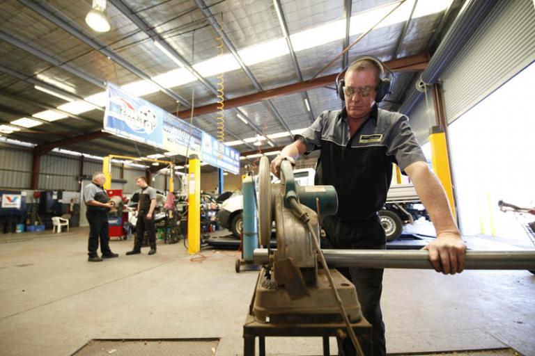 front view of auto mechanic cutting metal pipe with a metal grinding machine in the car servicing workshop