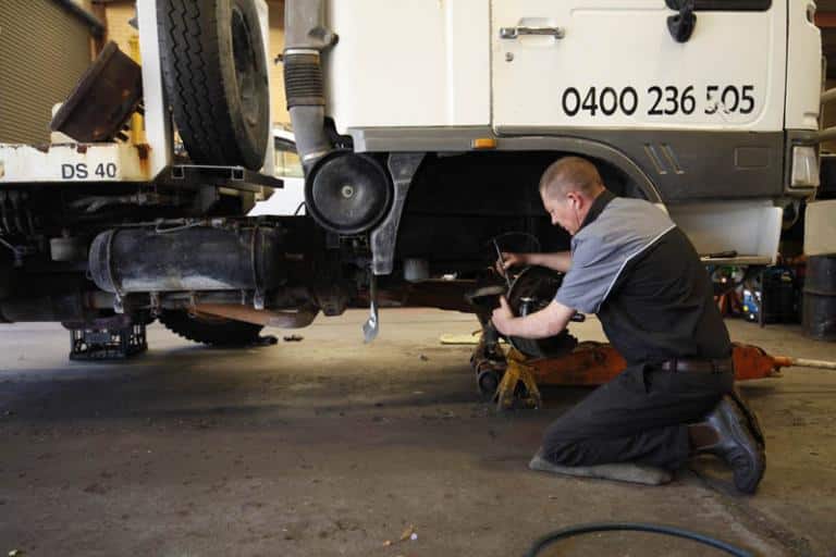 automobile mechanic repairing trucks brakes in the garage while truck is on a jack